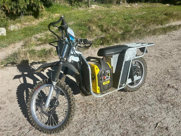 Galvbike carrying a portable generator in its centre load bay on a farm track